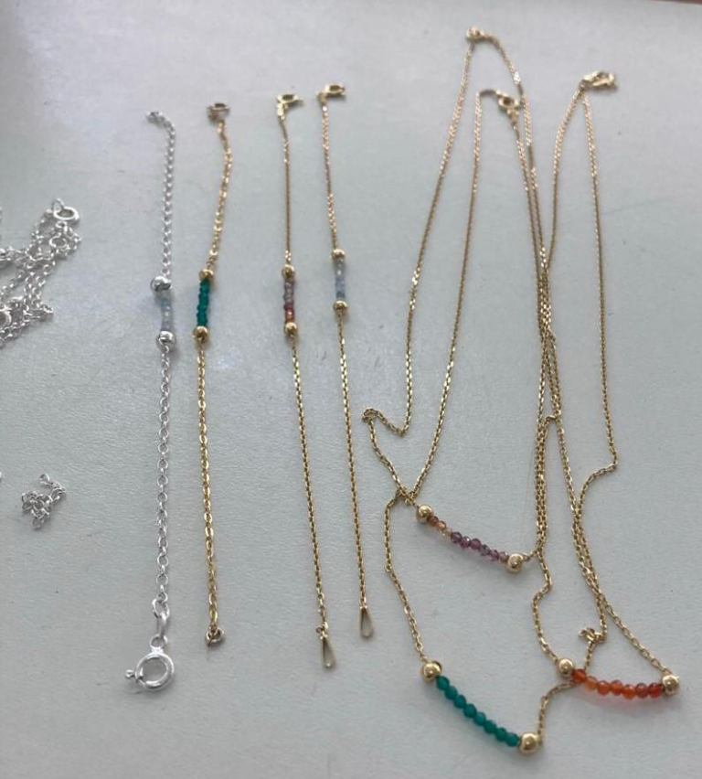Fine gold necklaces with small coloured gemstone sections arranged on a light surface